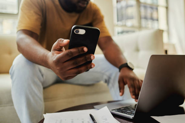istock A young black man sitting on his sofa  while texting on a mobile phone and  laptop computer . Stock photo, copy space 1502426085