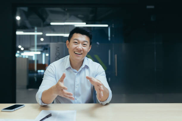 istock Smiling asian businessman talking on video call, looking at camera while sitting at desk in office. Gestures, discusses, explains 1502426516
