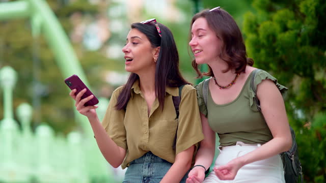 Two young women are using mobile phone outdoors in the public park