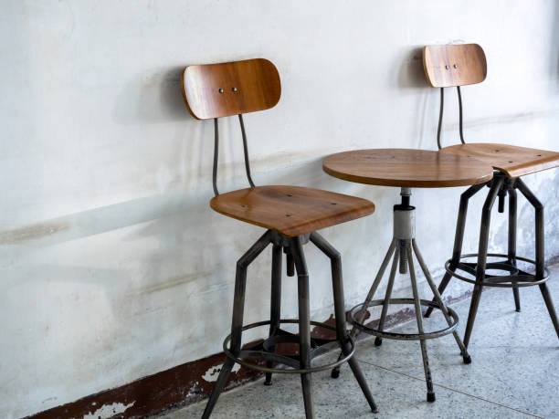istock Empty vintage spinning chairs backrest, seat and round spinning side table decorated on old white wall background, loft style building interior. Swivel wood table set, wooden and black iron materials. 1502431396