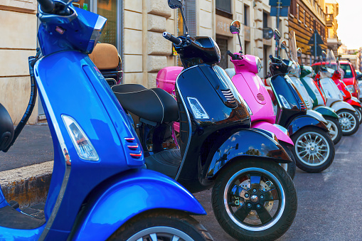 A series of multicolored Vespa scooters parked in a row along the street, scooter rental location in the city.