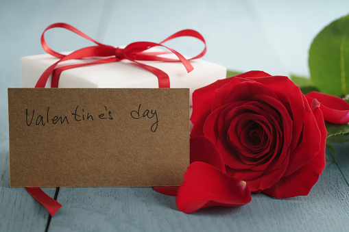 red rose on blue wood table with gift and valentines day paper card, shallow focus