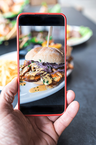 Food blogger using a smart phone taking photos of a delicious burger to share on social media