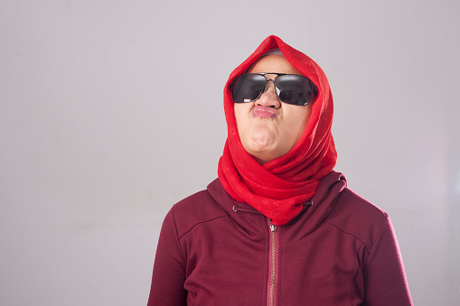 Portrait of muslim lady wearing black sunglasses in red suit and hijab smells something bad