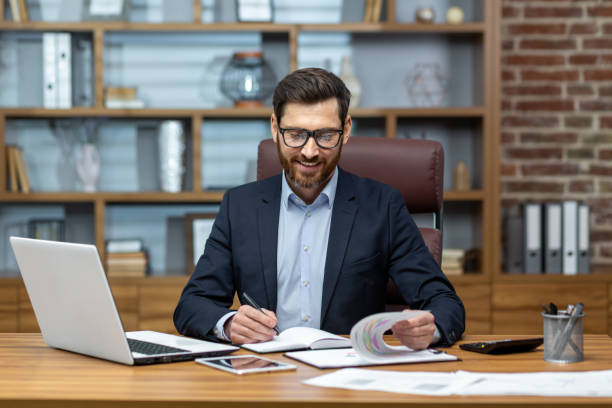 istock Mature businessman doing paperwork, man working with documents, contracts and bills sitting at table using laptop at work, financier accountant with beard and glasses 1502449982