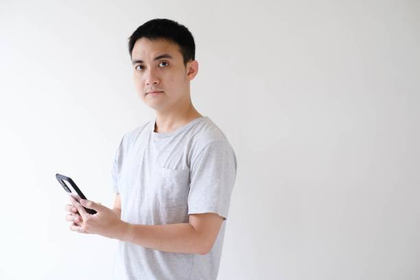 istock A young Asian man is holding a smartphone and looking at the camera 1502450251