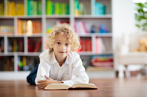 Child reading book. Kids read. Little boy at a colorful bookshelf doing homework for school. Student with books. Early education and development. Home library for children. Preschool kid study.