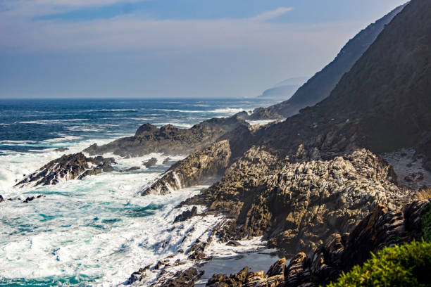 mare agitato e onde che si infrangono contro la costa rocciosa e le scogliere della costa di tsitsikamma lungo la garden route, in sud africa. - weather vane foto e immagini stock