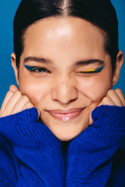 Wearing vibrant eye makeup, woman winks at the camera in a studio