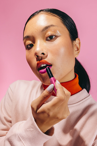 Portrait of a young woman applying a two-toned lipstick, she looks at the camera with confidence. Woman creating a trendy, bold look on her face with self-assurance.