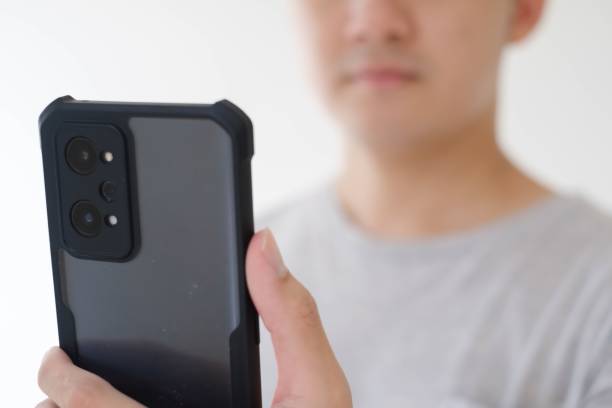 Close-up shot of the partial face of a young Asian man who wears a grey t-shirt is holding and looking at a smartphone. Focused on the phone. Shallow depth-of-field. Isolated white background.