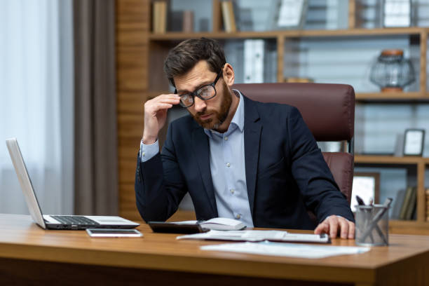 istock Upset businessman behind paper work inside modern office, mature man with beard reading financial reports and account documents unhappy with results and disappointed with achievements 1502453327