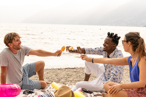 Three adults on the beach by the lake eating an ice cream