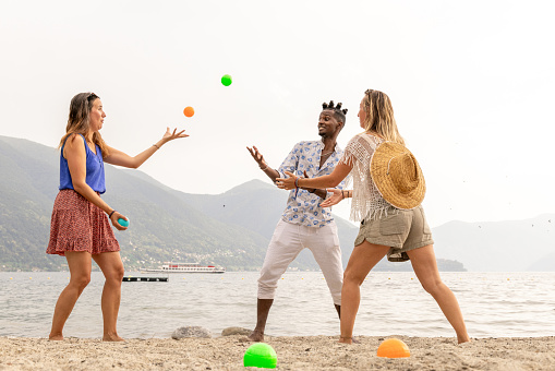 Three adults playing boules on the beach by the lake. Two women and a man.