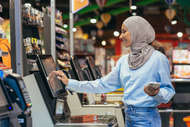 una mujer compradora en un supermercado con un hijab paga los productos en una caja de autoservicio, un servicio conveniente para los clientes - turkish ethnicity white black contemporary fotografías e imágenes de stock