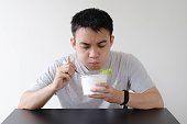 A young Asian man is eating food on a disposable white paper bowl with a chewing mouth