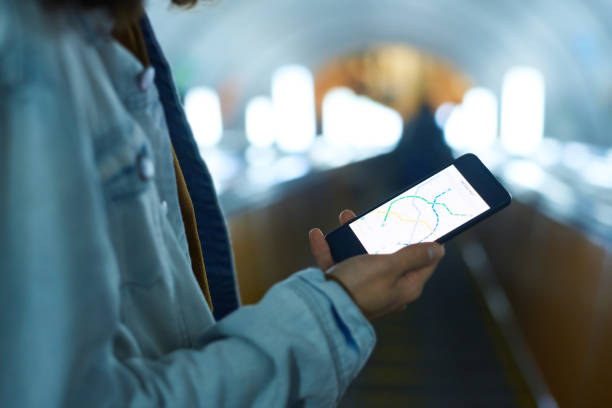 Close-up of boy in blue denim jacket holding smartphone with metro route map on screen while standing on escalator and moving downwards