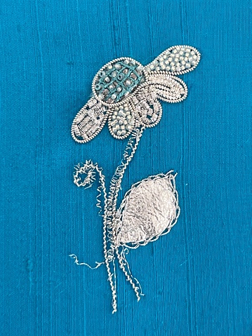 An embroidered daisy using silver work technique. Stitched on to a turquoise silk dupion background
