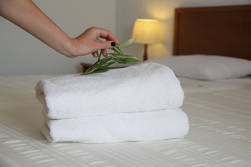 Room service. Woman changing towels in hotel room. Housecleaner putting towels on the bed, preparing everything for clients to move in