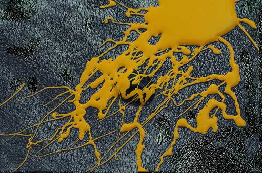 splashes of thick yellow ink stains on the surface of a gray cloth with coarse fibers. screen printing ink