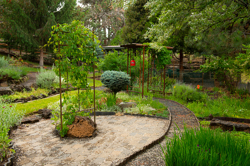 A small estate landscaped garden the lush trees, paths and a red accent hanging bell chime  in Bend, Oregon