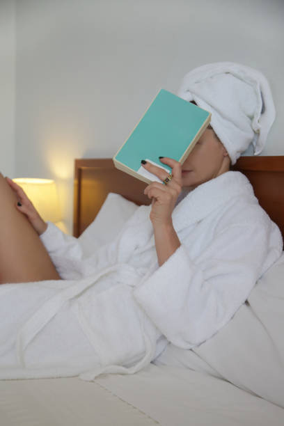 istock Young woman in bathrobe holding book in bed 1502463902