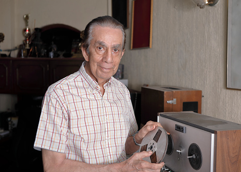Senior man happily looking at camera holding a reel to reel audio tape.