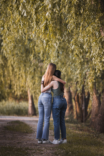 An eternal embrace: Friendship and happiness in nature. In this beautiful photograph, we capture a magical moment where two friends embrace lovingly on a picturesque path surrounded by majestic trees. The serene ambiance of nature enhances the emotion of the scene, conveying the powerful concept of friendship and shared happiness.