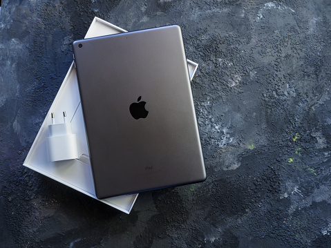 Lleida, Spain - February 28, 2023 : Studio photo of the new gray Apple iPad, logo from rear view and charger . Isolated on gray background. Illustrative editorial content.