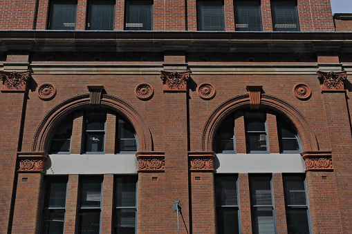Red brick facade of historic, heritage-listed building from AD 1895 on Campbell Street in the CBD with arched bays, stone cornices and strings, terracotta capitals and rosettes. Sydney-NSW-Australia.