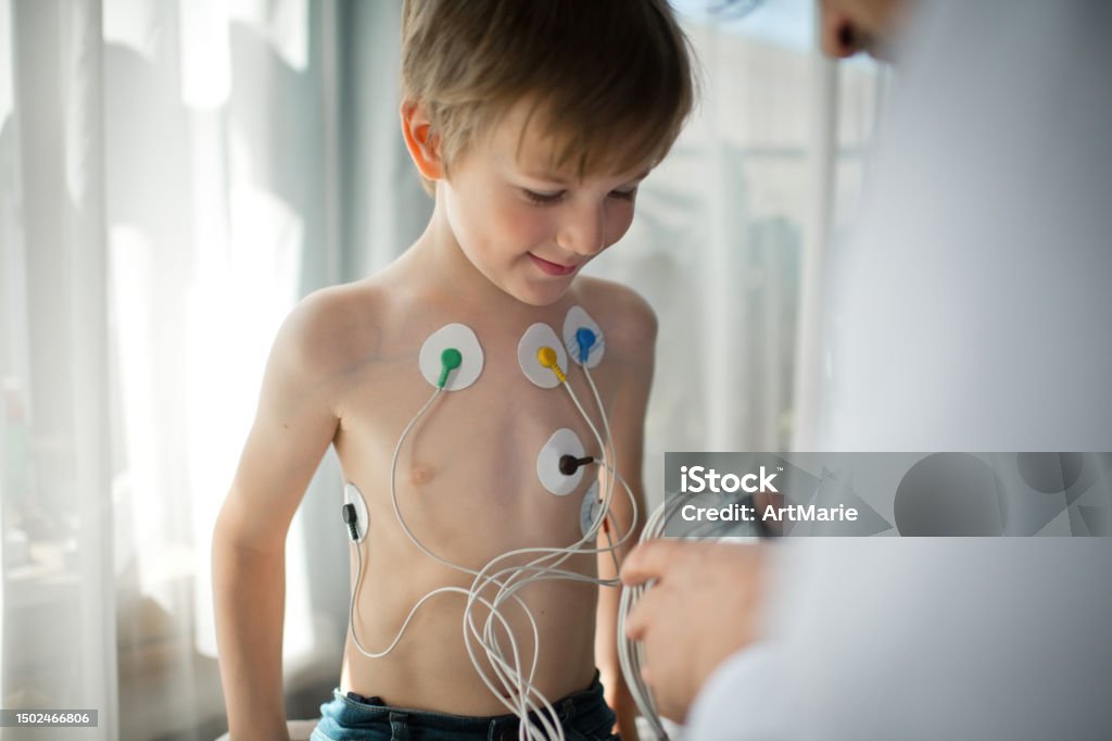 Doctor adjusting  ECG holter monitor for a child to check his heart health Little boy at a doctor's office Electrocardiography Stock Photo