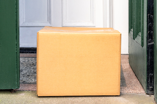 A blank cardboard box delivery left in the front porch of a house.