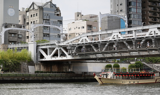 May 26, 2023 - Taito City, Japan: A tour boat passes under the Sumida River Walk between Taito City to the west and Sumida City to the east. Residential buildings line the Hanakawado area.