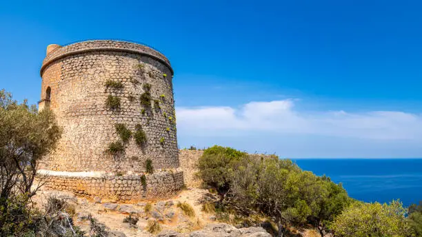 Old Torre Picada tower standing tall on the cliffs of Port de Sóller with great view to the mediterranean sea, transporting the viewer to a bygone era of fortifications and coastal defense in Mallorca