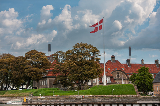 Copenhagen, Denmark - September 14, 2010: East shore harbor with historic marine grounds and brick, red-roofed buildings, now museum under blue cloudscape. Green lawn and foliage