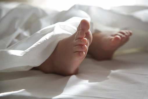 Child feet under the white blanket under soft morning light