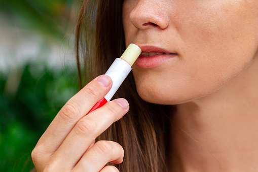 Applying hygienic lipstick to moisturize dry lips close up outdoors. Lips care
