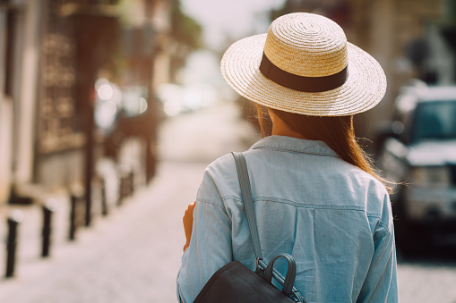 Woman traveler in hat and with backpack relaxing and walking along the street of a european city. Vacation and traveling lifestyle