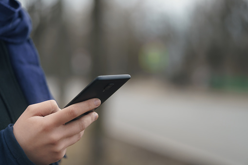 female teen hand using smartphone outddor on empty town street in spring morning, closeup photo