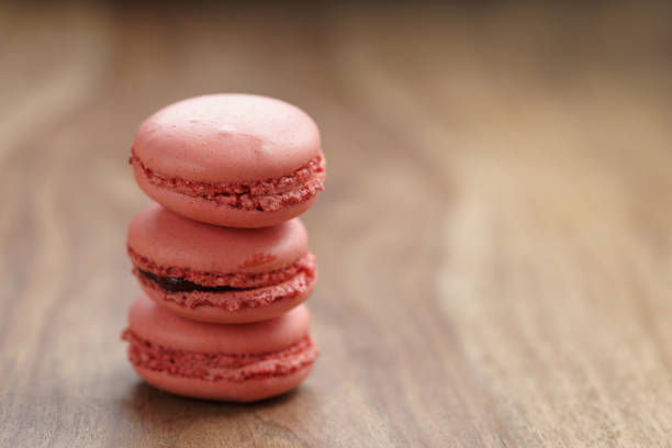 closeup shot stack of pastel colored macarons with strawberry flavour on wood table, copy space