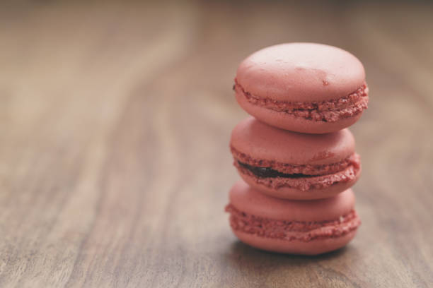 closeup shot stack of pastel colored macarons with strawberry flavour on wood table, vintage toned photo