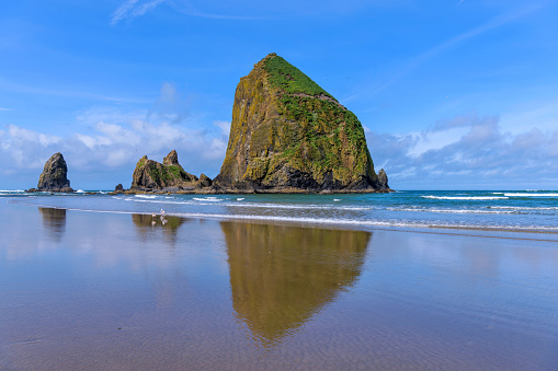 A sunny Spring morning view of famous Haystack Rock reflecting on smooth sandy Cannon Beach. Oregon, USA.