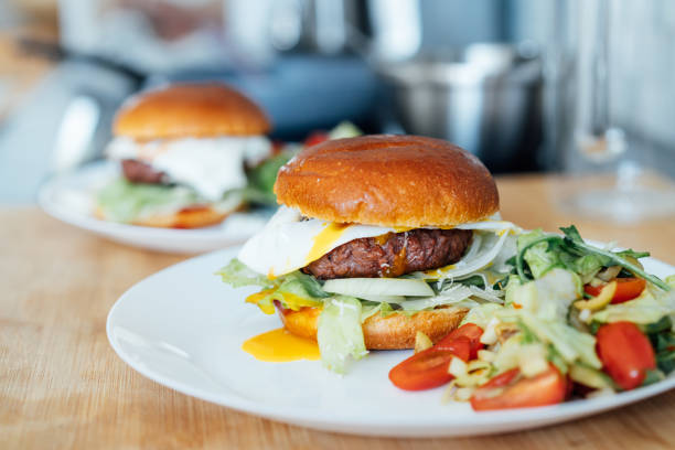 istock Closeup homemade burger with artificial meat, fried egg and vegetables on white plate with fresh salad on the kitchen table. Healthy fast food cooking recipe at home. Vegetarian diet. Selective focus. 1502531081
