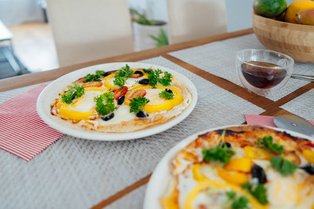 Fresh homemade breakfast pizza on bread wrap with eggs, cheese, tomatoes, bell pepper and herbs on the served table. Tasty and healthy ideas for breakfast at home. Soft selective focus
