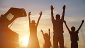 Parents and kids raising hands to sky enjoy summer sunset