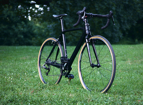 black bicycle in field of grass (modern road bike with drop handlebars, skinwall tires) cyclocross gravel bike monotone, sleek, fresh build (700c wheels, double crankset, cantilever brakes, shifters)