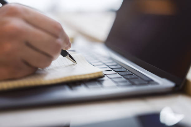 istock Sharp view of a woman's hand transcribing in a notepad on a cutting-edge laptop, with a defocused backdrop 1502537367