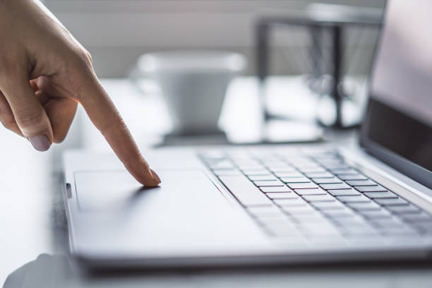 写真は、スタイリッシュなラップトップのキーボードで入力する女性の手を捉え、オフィスの周囲が背景にぼやけて見える - mail keyboard button ストックフォトと画像