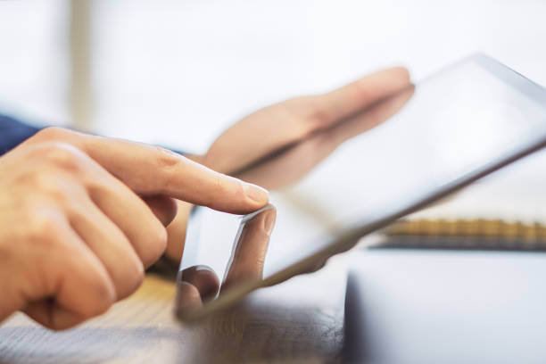 istock Male hand engaging with a cutting-edge digital tablet, device resting on a desk against the unfocused hustle of a sunlit office 1502537520