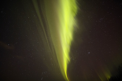 A closeup of aurora bore with a mountain and the moon in the distance